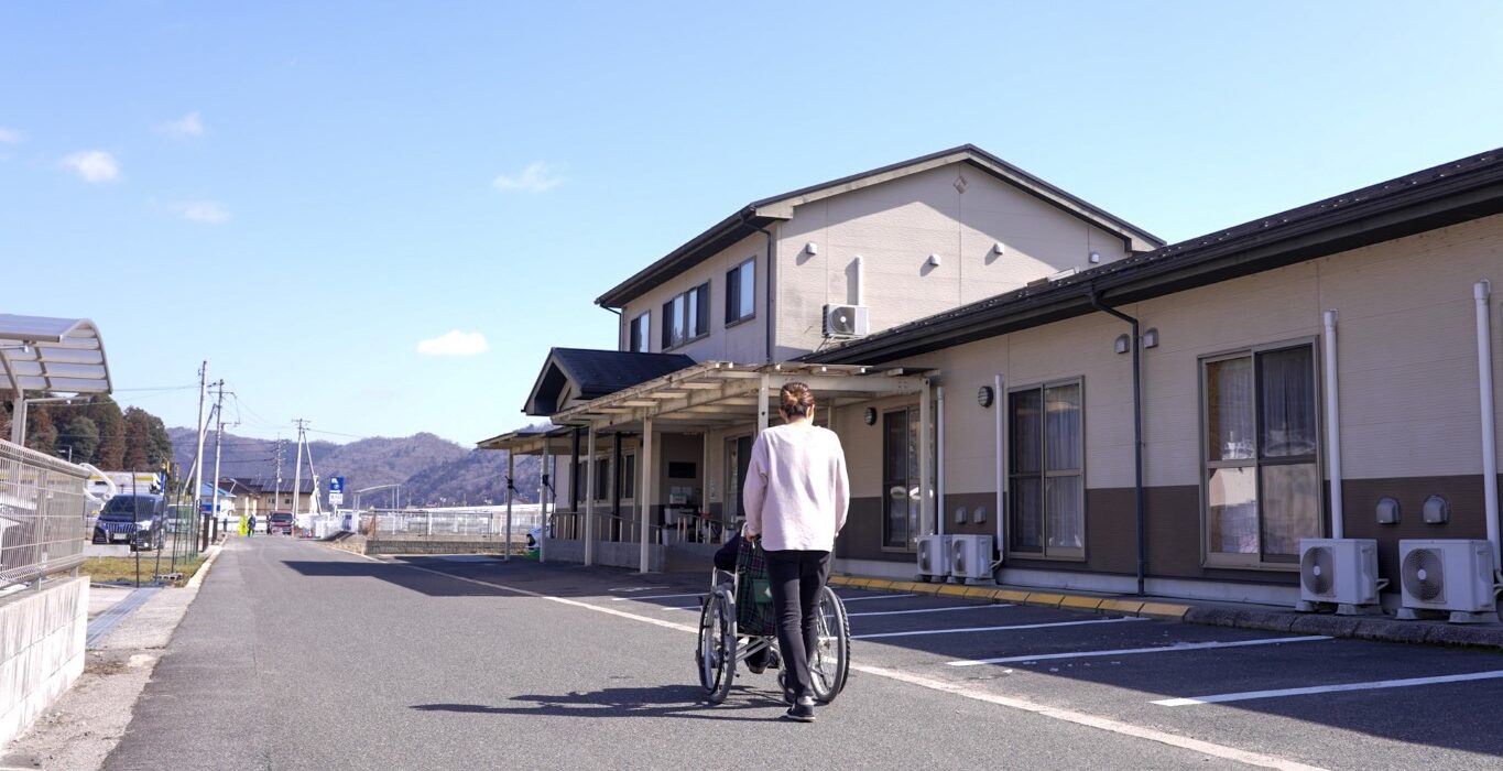 介護施設の建物外観。入居者が自転車で敷地内を移動している風景。